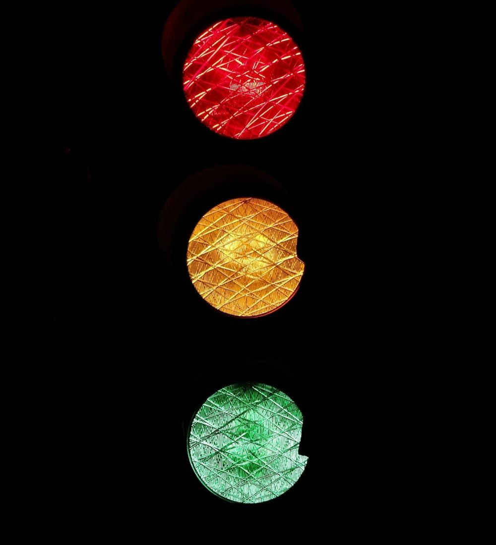 Vivid image of red, yellow, and green traffic lights against a dark background.